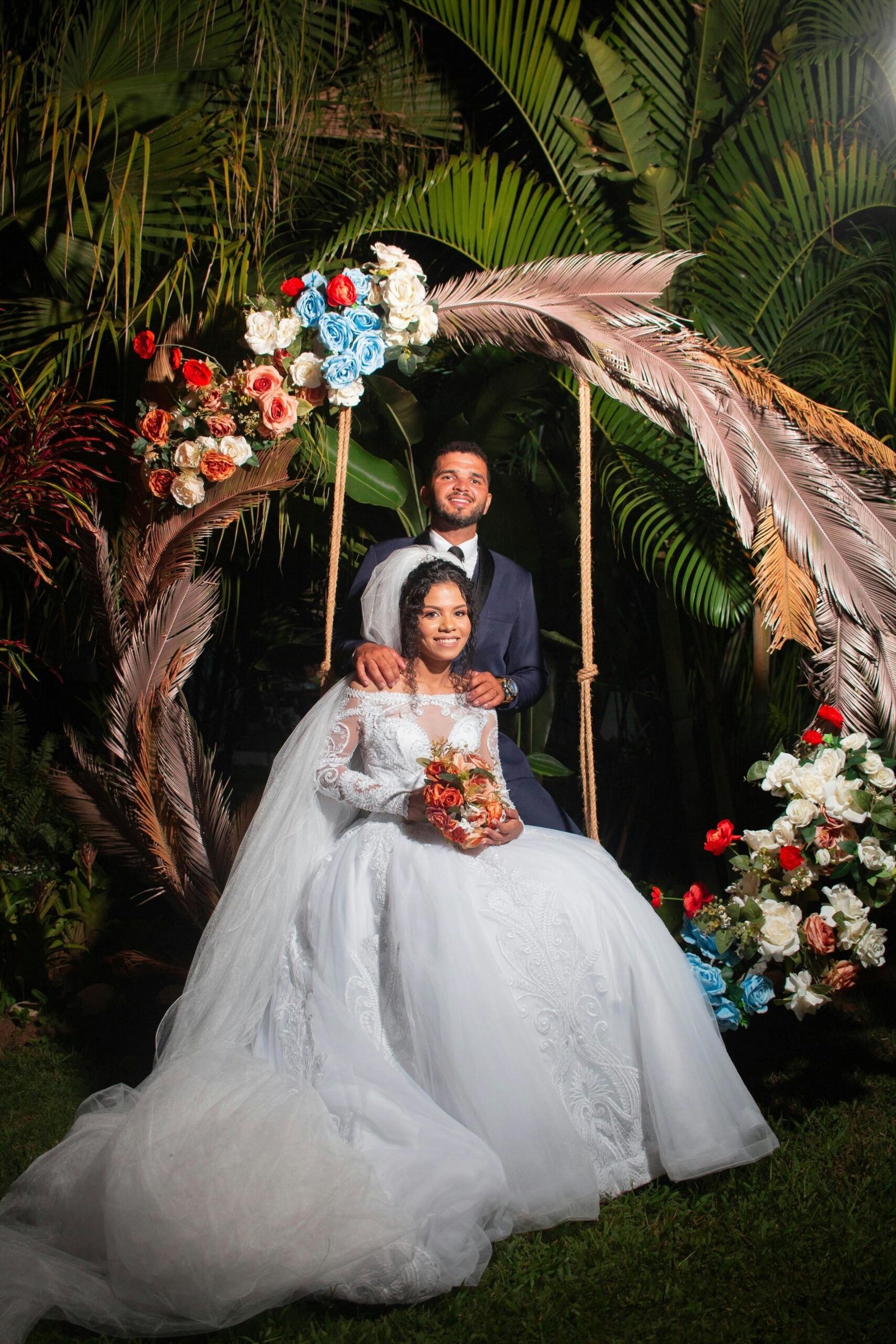 A bride and groom pose elegantly under a floral arch at their outdoor wedding ceremony.